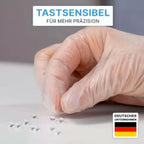 Eine hand in einem transparenten puderfreien vinylhandschuh von arnomed hält kleine glänzende silberne perlen