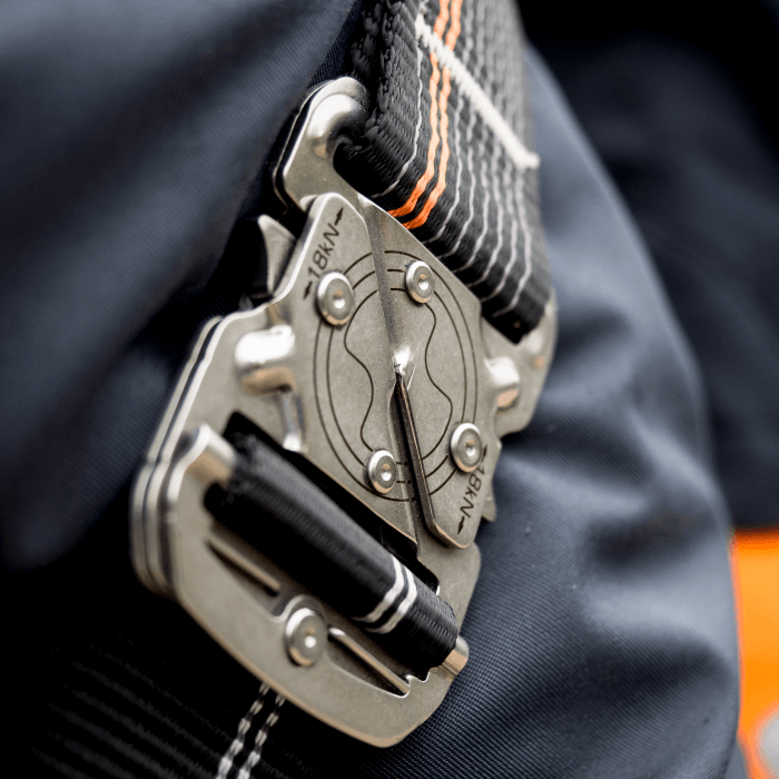 Silberner metallkarabiner mit schwarz-orange gestreiftem gurtband am skylotec ignite trion sicherheitsgurt