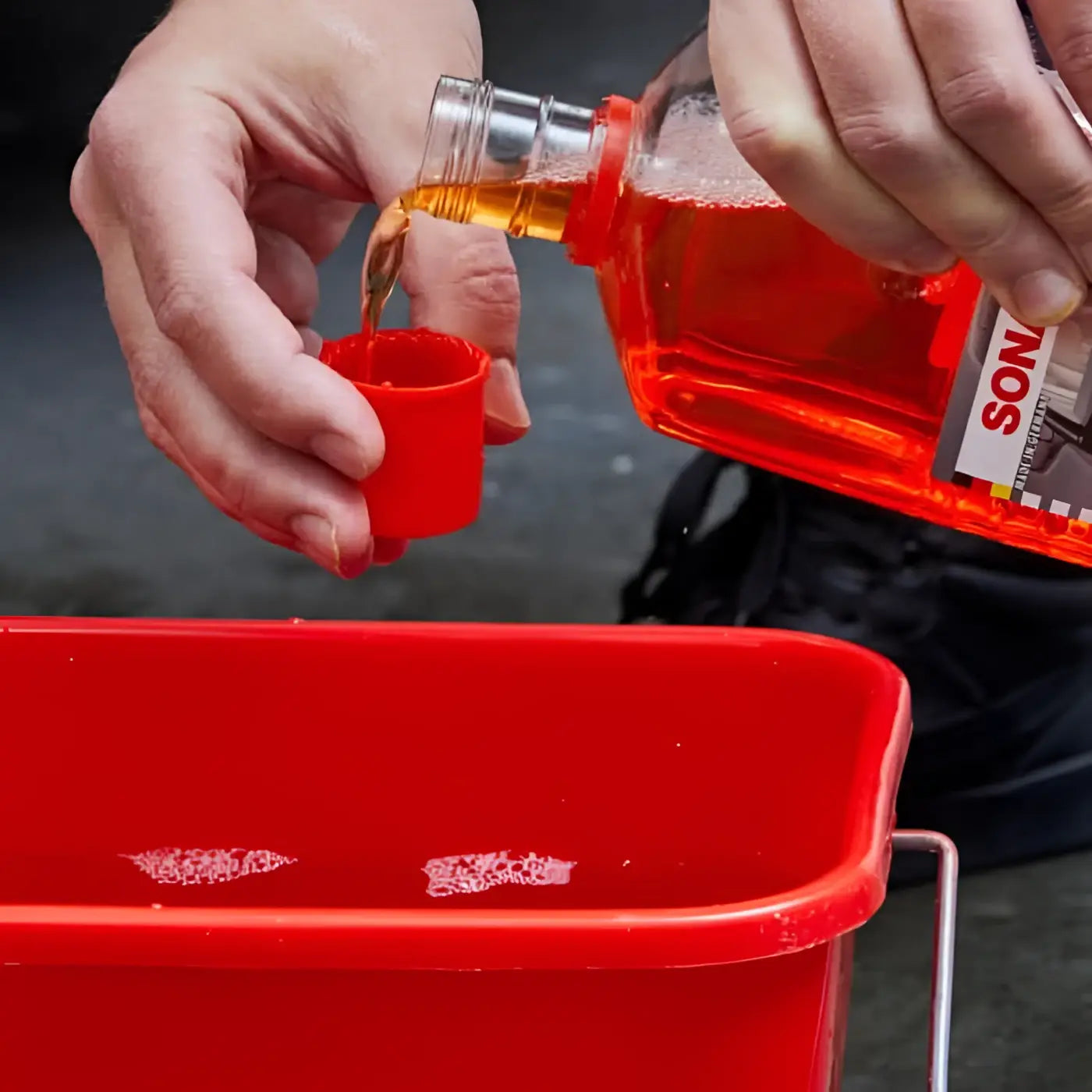 Rote plastikflasche mit silbernem verschluss labeled sonic gefüllt mit orangefarbener flüssigkeit sonax autoshampoo konzentrat 2l