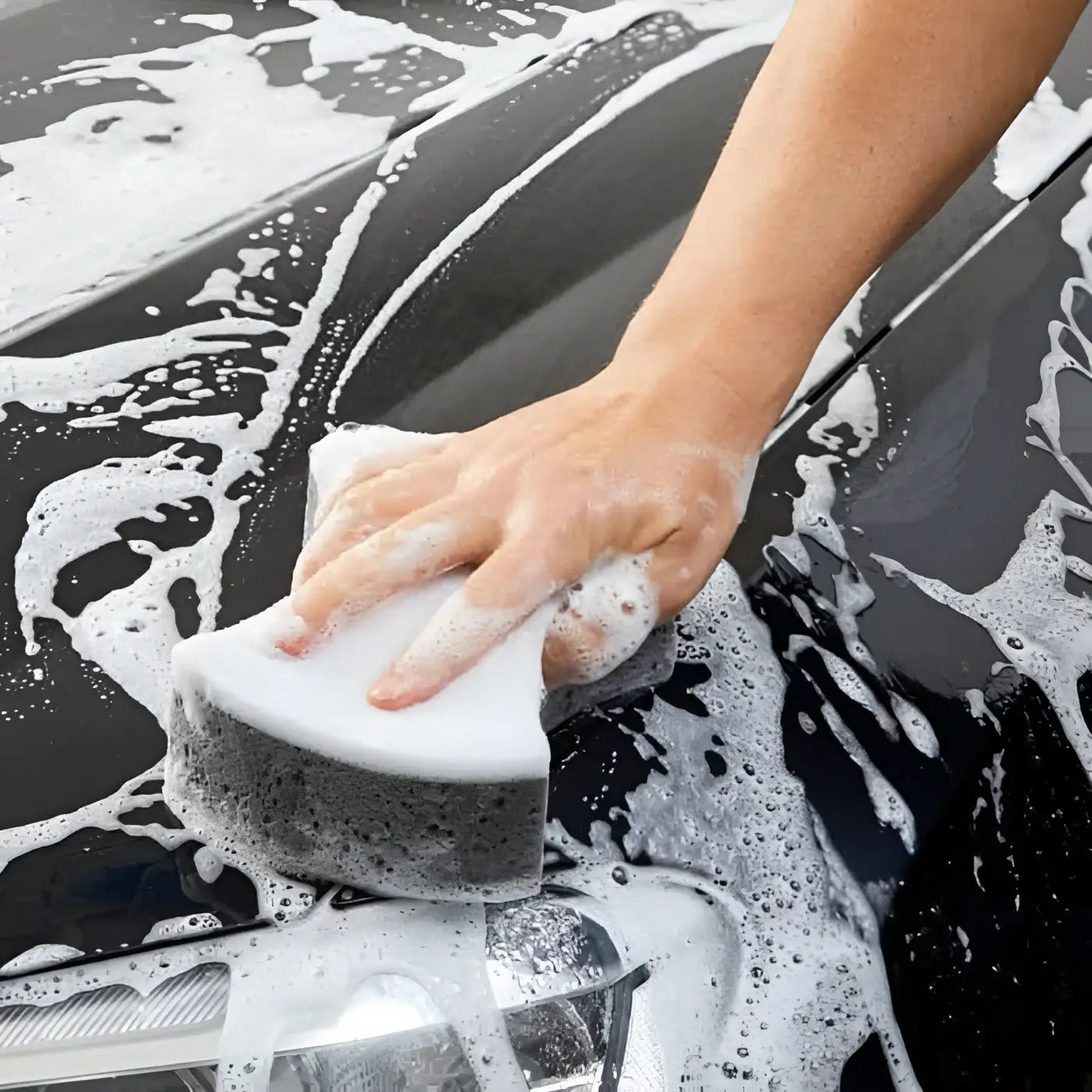 Weiß-grauer schwamm wird zum waschen der schwarzen oberfläche mit sonax autoshampoo konzentrat 2l verwendet