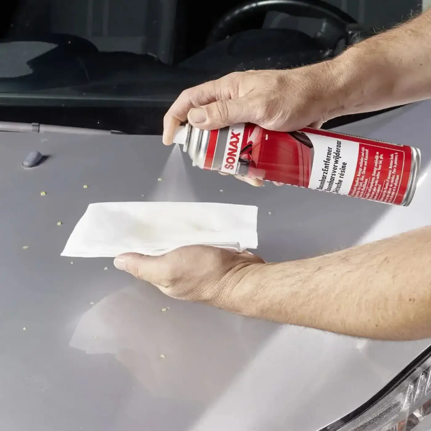 Hand hält rote und silberne sonax baumharzentferner spraydose 400ml zur autowachspflege