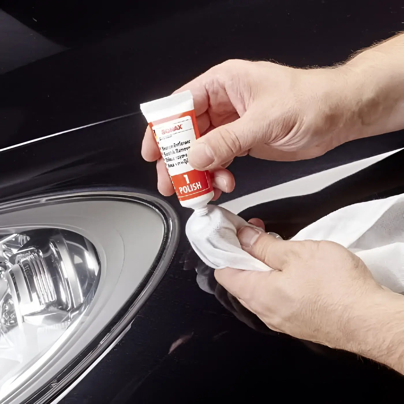 Rote und weiße sonax kratzerentfernerset lack tube wird mit kloth auf schwarzer fahrzeugoberfläche aufgetragen