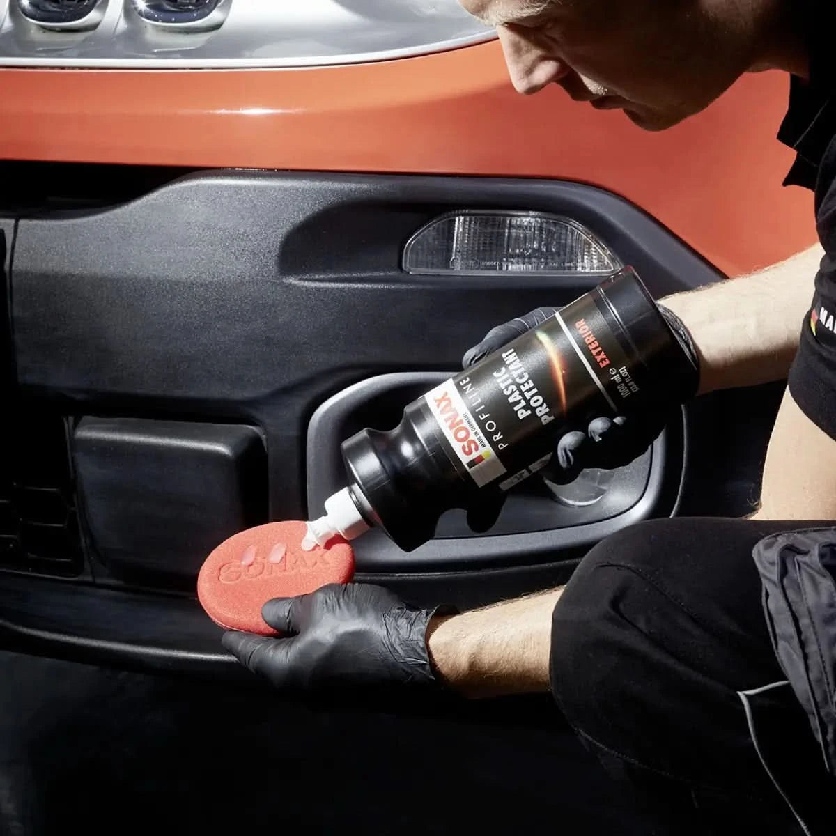 Schwarze flasche isonik plastic protector extreme mit weißer düse wird auf rotes rundes applizierpad für sonax profiline plastic protectant exterior dosiert