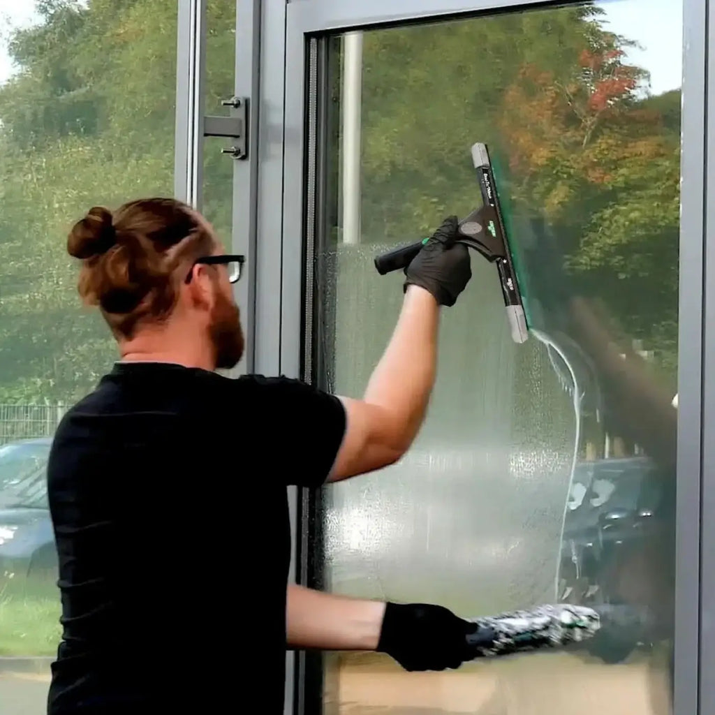 Schwarze gummihandschuhhand hält ungger ergotec ninja starter fensterputzer-set 2in1 squeegee mit grünem blatt